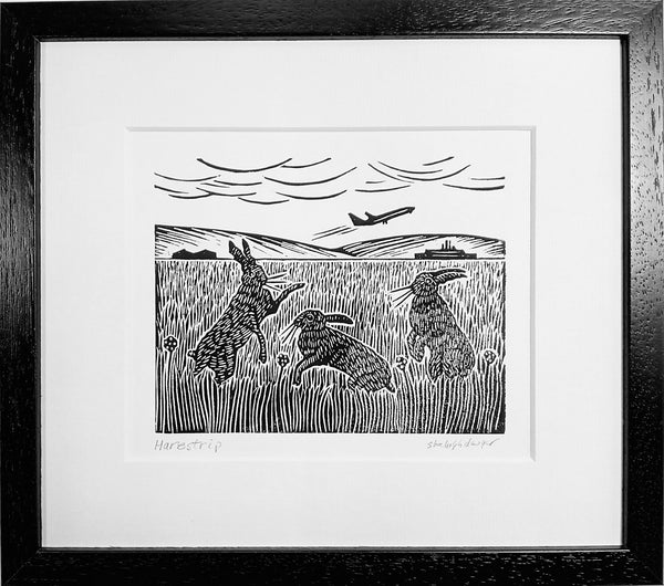 Framed lino print in black ink of hares playing at an airstrip