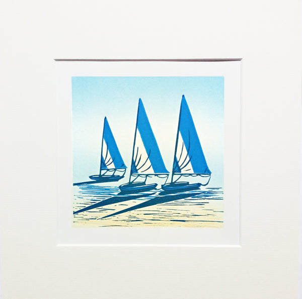 Mounted linocut in blue, yellow and black ink of sailing boats on the shore