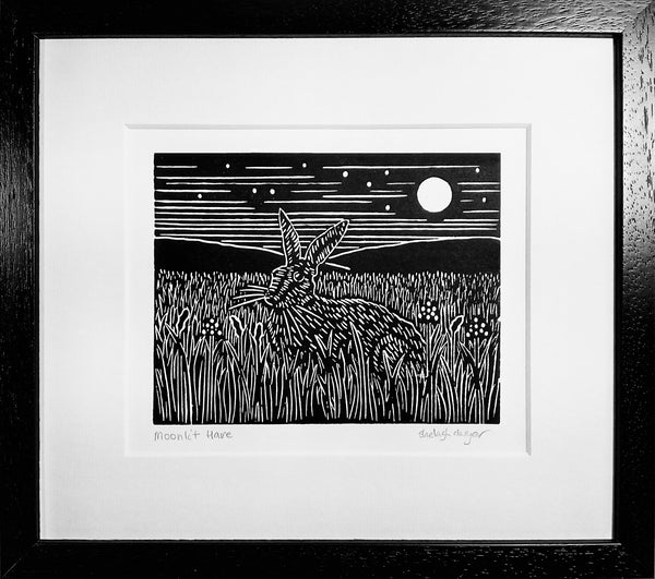 Framed linocut in black ink of hare on grass under moonlit sky 