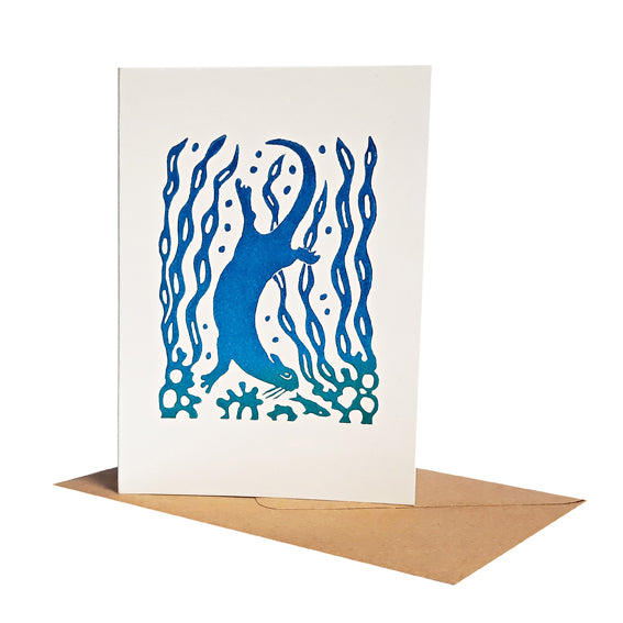 An Otter follows a fish amongst seaweed printed from a linocut with blue ink. Suitable as a greeting or notecard.