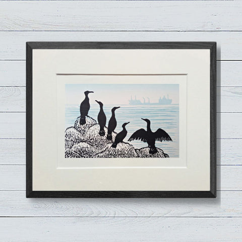 Lino print in black and blue grey ink of cormorants on rocks with cargo ship in the distance