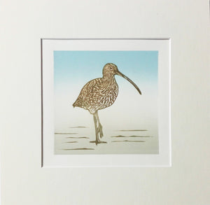Mounted linocut of a curlew standing on the shore
