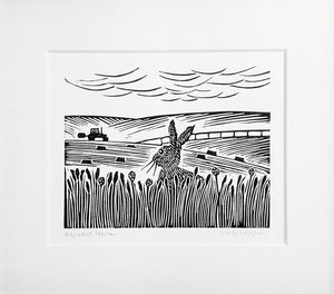 Mounted lino print in black ink of hare gazing at tractor working in a field in the distance