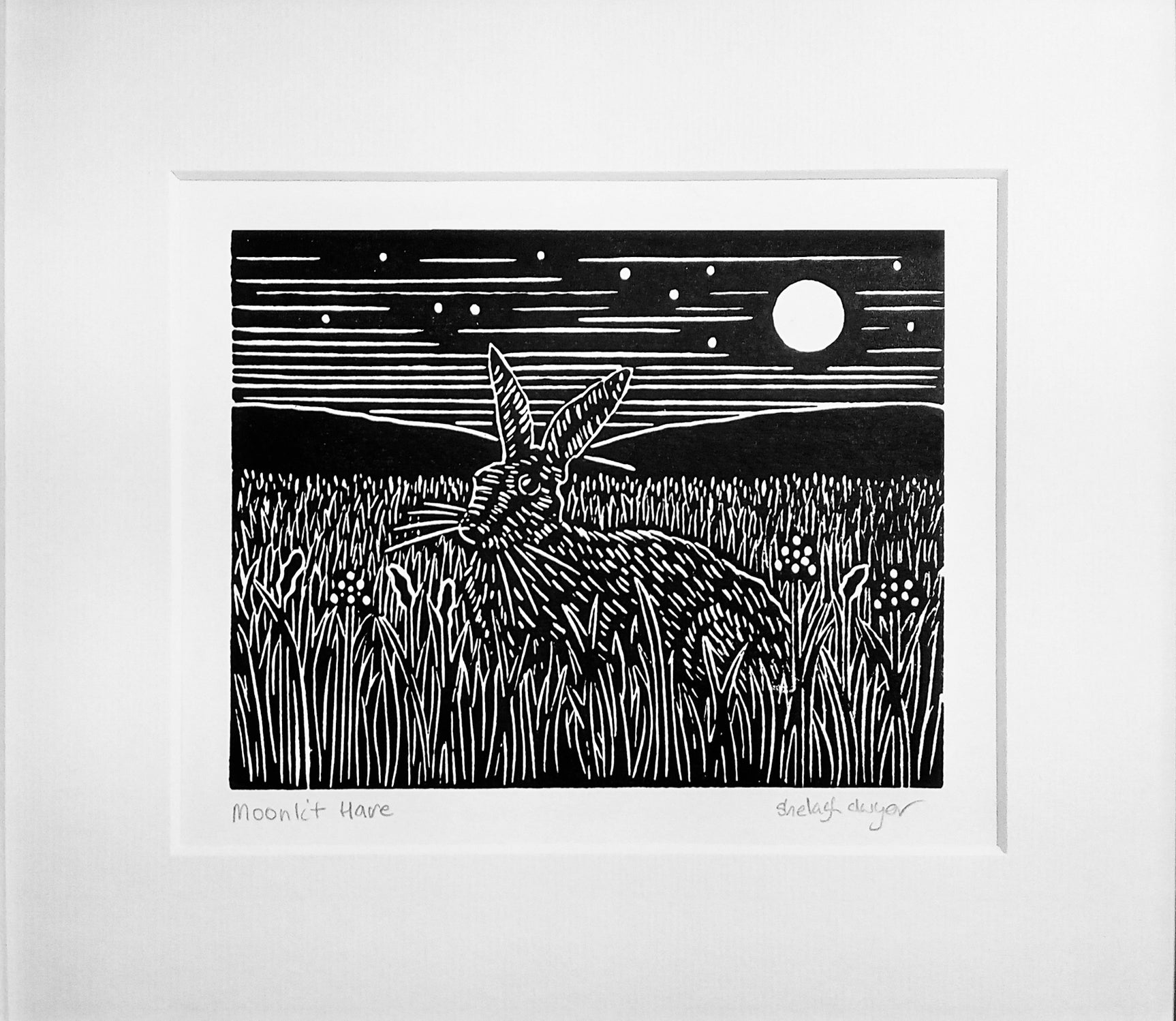 Mounted lino print in black ink of alert hare sitting on grass under starry moonlit sky
